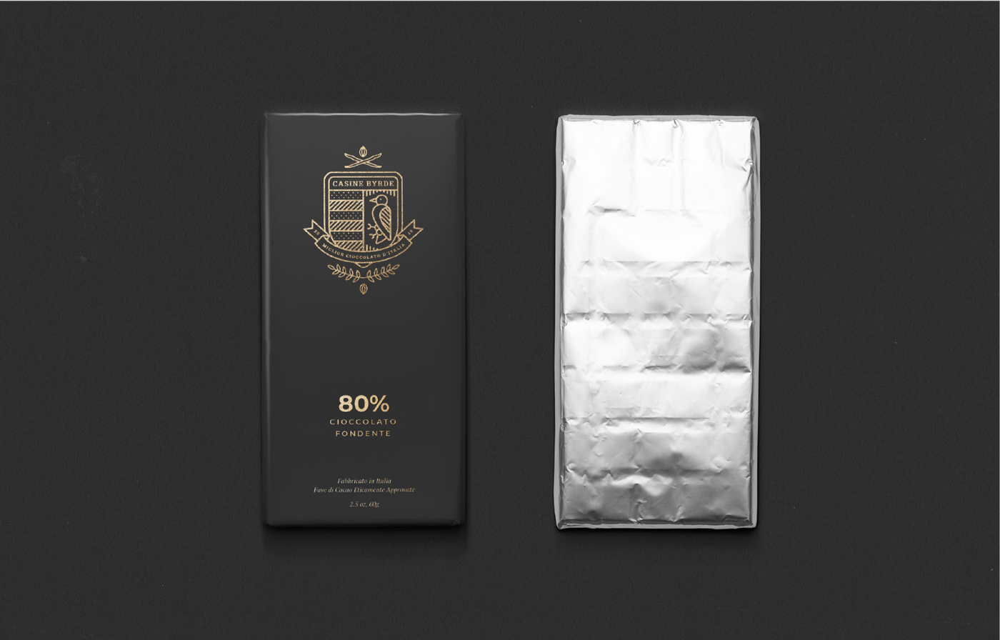 A dark chocolate bar in elegant black and gold packaging is shown next to the unwrapped bar covered in silver foil, both placed on a black surface. The package reads 80% Cioccolato Fondente.