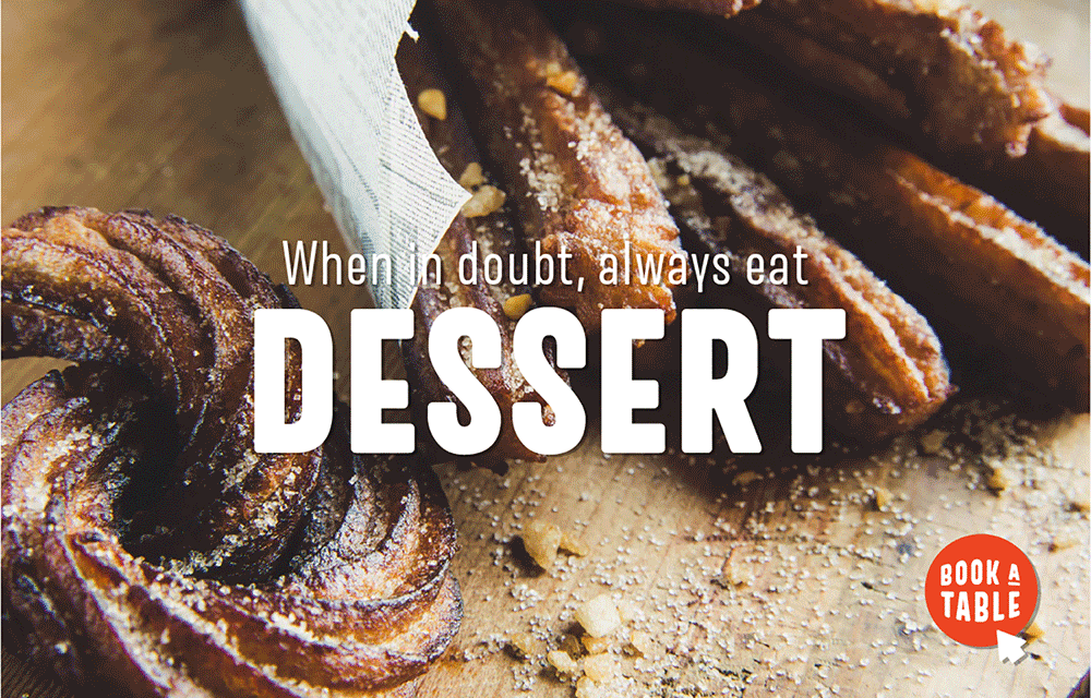Close-up of churros sprinkled with sugar on a wooden surface. Overlaid text says, When in doubt, always eat DESSERT. A red button in the corner reads, BOOK A TABLE.