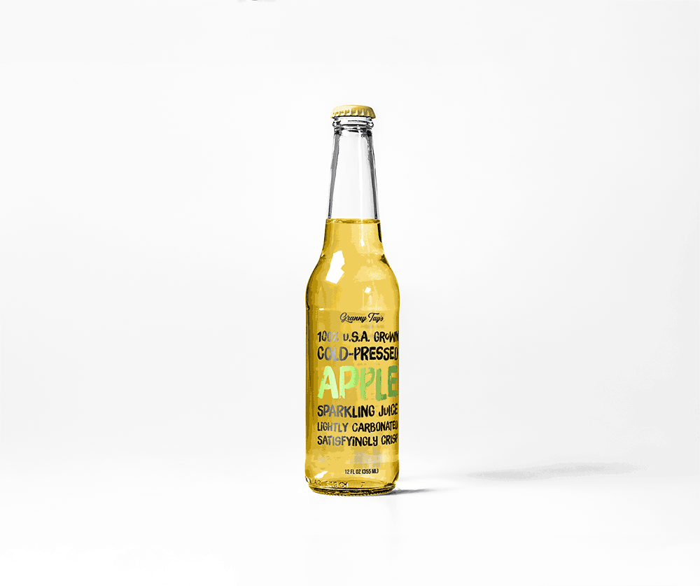 A clear glass bottle of sparkling apple juice with a yellow cap, filled with light golden liquid. The label reads, 100% USA Grown Cold-Pressed Apple Sparkling Juice in bold green and yellow letters designed by Sandra Tay.
