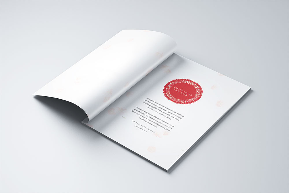 An open booklet lying on a light surface, displaying a page with a large red circular stamp-like design and text printed below it. The adjacent page is blank.
