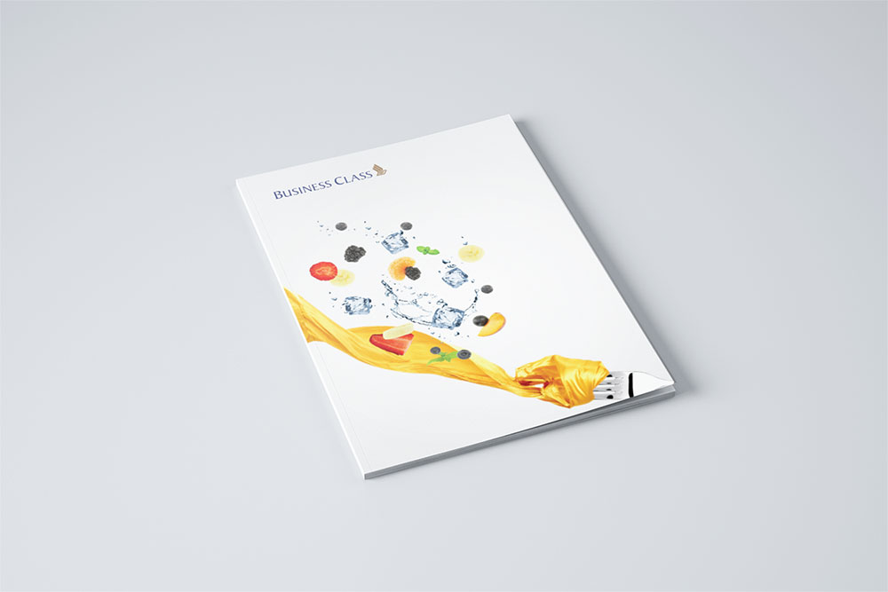 A business class menu for SIA designed by Sandra Tay with a white cover featuring food ingredients, ice cubes, and a yellow cloth swirling from a fork, arranged artistically against a light grey background.