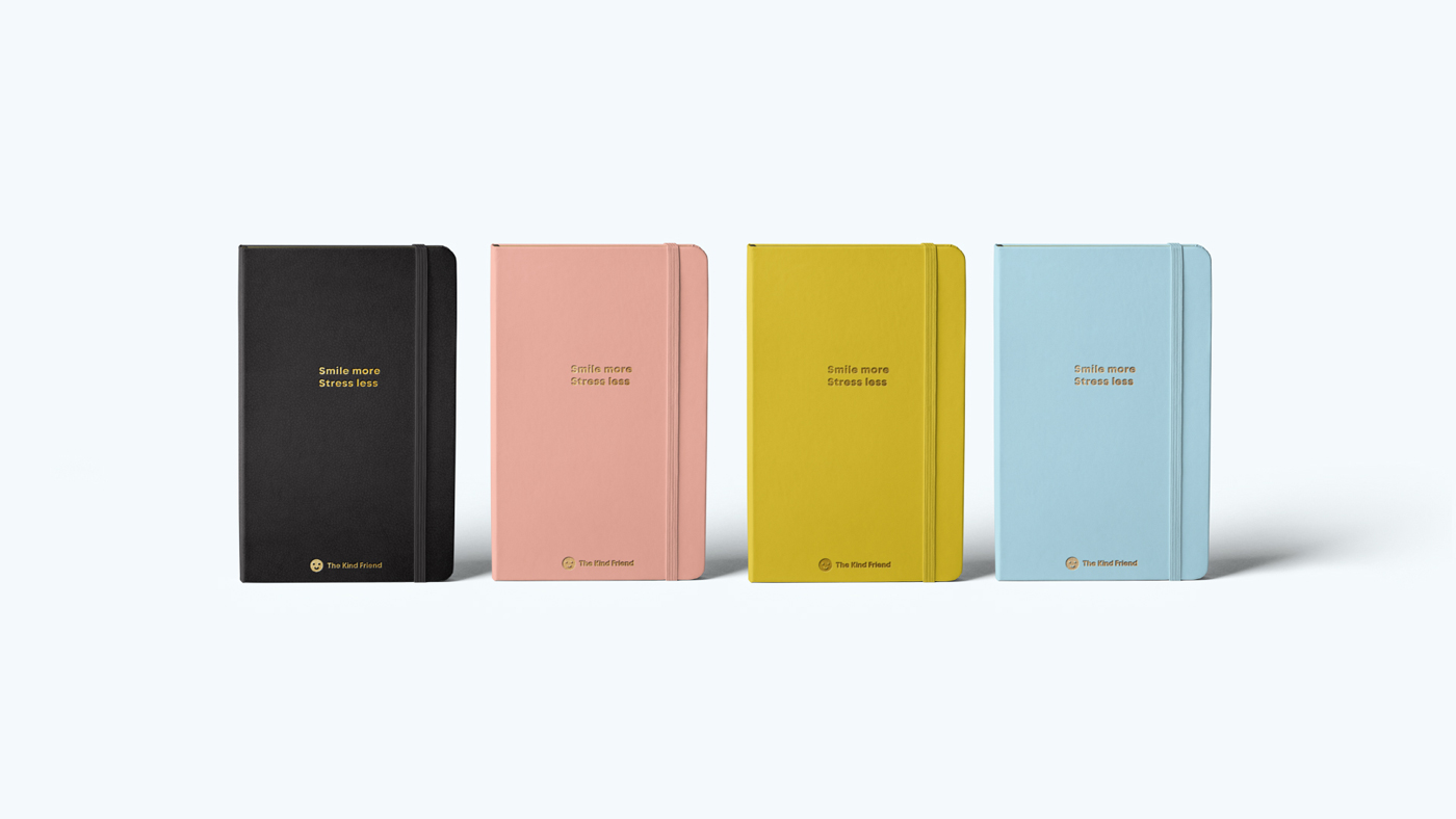 Four hardcover notebooks in black, pink, yellow, and blue, each with the phrase Smile more. Stress less. embossed in gold on the front cover, displayed upright against a light background.