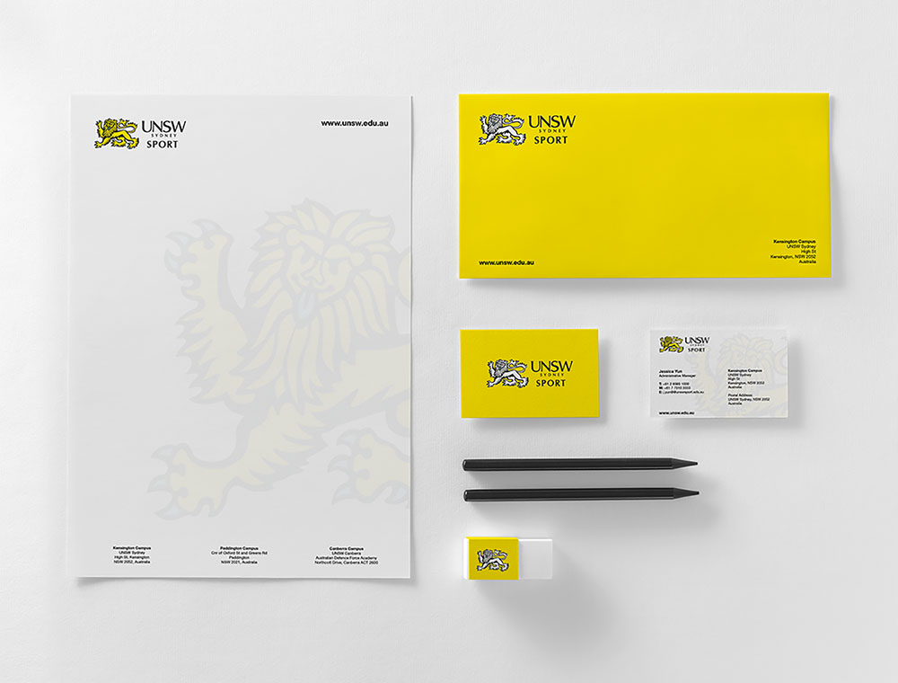 UNSW Sport branded stationery set designed by Sandra Tay including letterhead, envelope, business cards, two black pencils, and an eraser, all featuring a yellow and black lion logo on a white background.