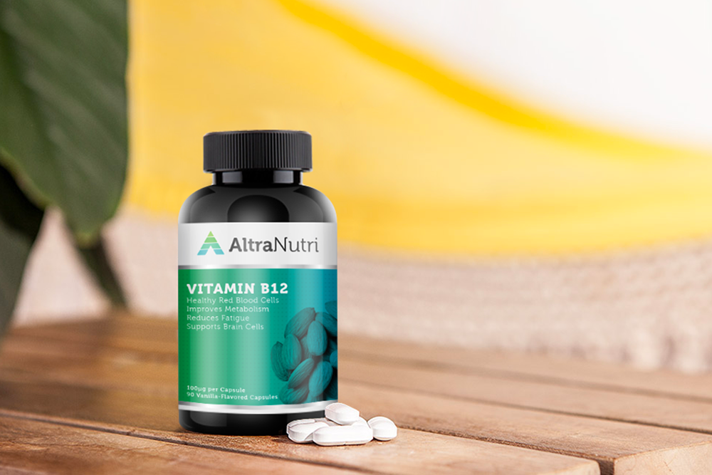 A bottle labeled AltraNutri Vitamin B12 sits on a wooden surface with several white capsules nearby; a soft-focus yellow and white background is visible.