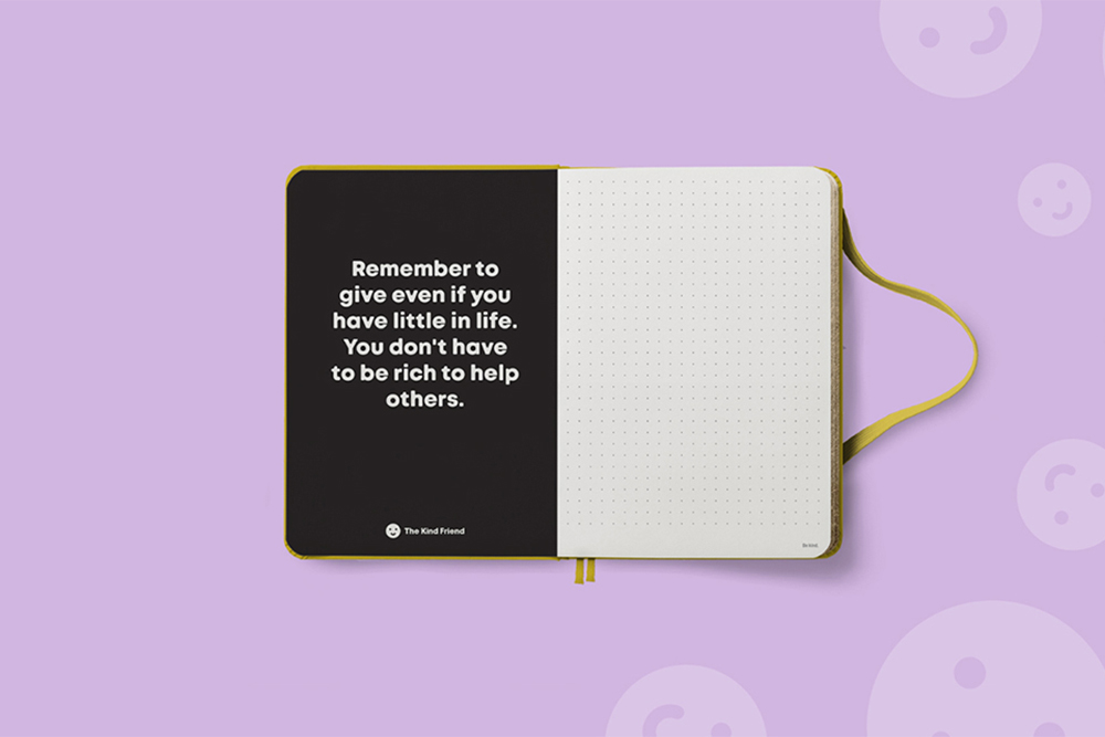 An open notebook on a lavender background. The left page is black with white text that reads, Remember to give even if you have little in life. You dont have to be rich to help others. The right page is blank and dotted.